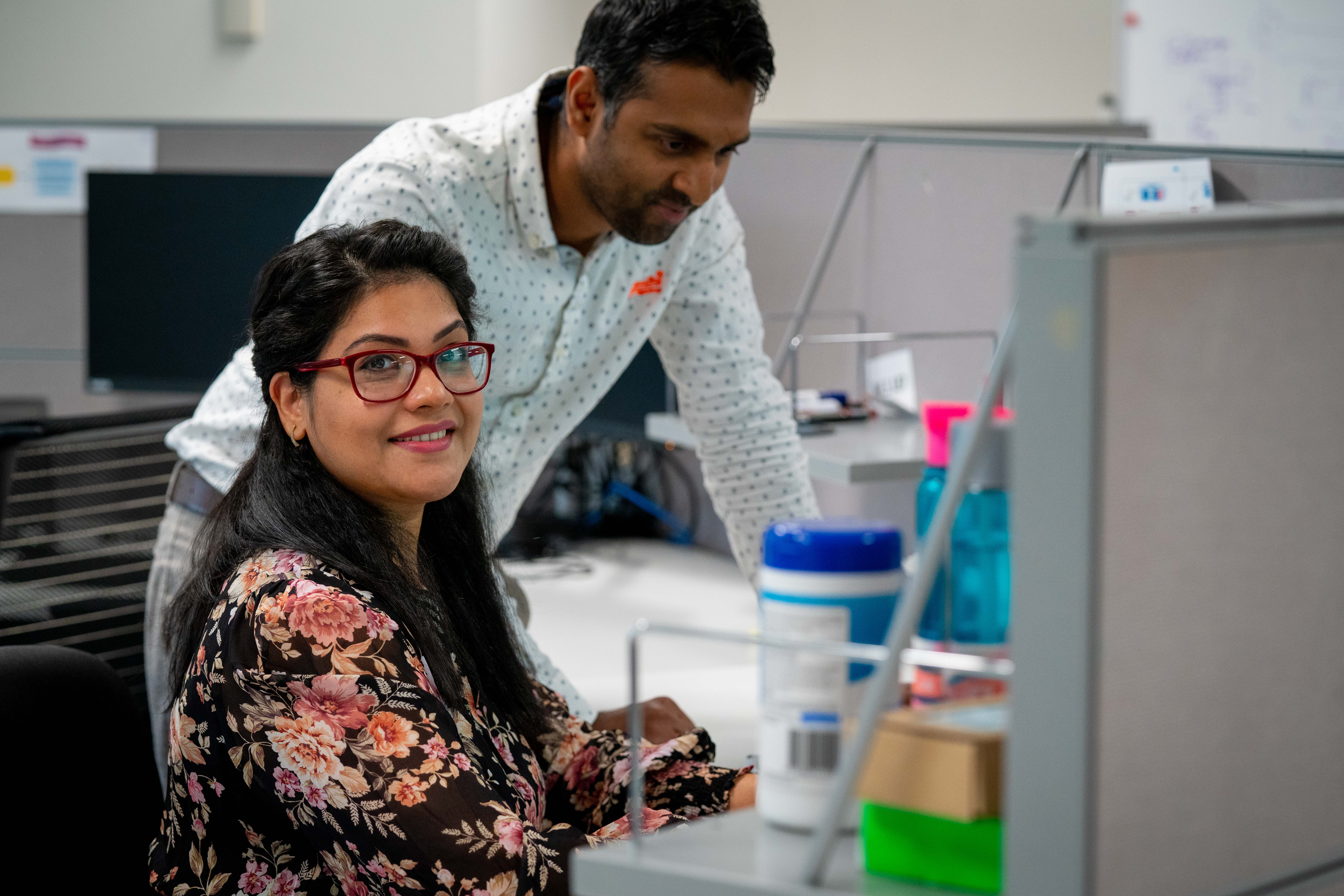 woman and man in an office cubicle. woman smiling at camera